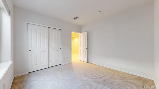 unfurnished bedroom featuring baseboards, visible vents, a closet, and light colored carpet