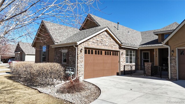 view of front facade with a garage, stone siding, driveway, and roof with shingles