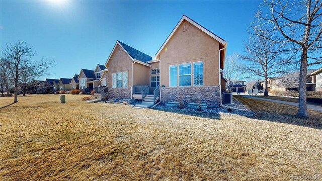 back of house featuring cooling unit, stone siding, a lawn, and stucco siding