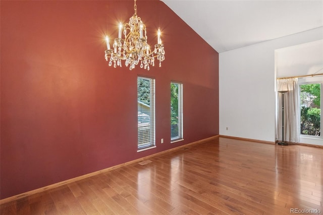 spare room featuring an inviting chandelier, vaulted ceiling, and hardwood / wood-style flooring