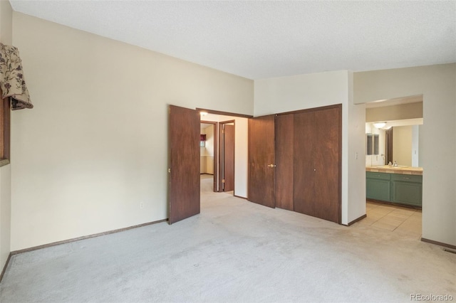 unfurnished bedroom with a closet, a textured ceiling, ensuite bath, light carpet, and sink