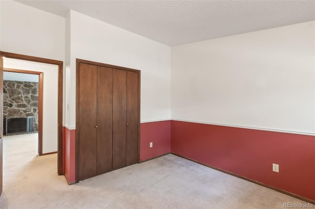 unfurnished bedroom featuring a closet, light colored carpet, a fireplace, and a textured ceiling