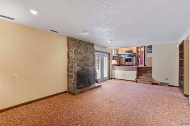 unfurnished living room featuring french doors, a textured ceiling, a fireplace, and light carpet