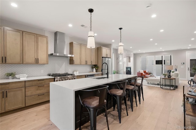 kitchen featuring a kitchen bar, wall chimney range hood, a kitchen island with sink, and light wood-type flooring