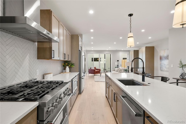 kitchen featuring sink, stainless steel appliances, wall chimney range hood, light hardwood / wood-style floors, and decorative light fixtures