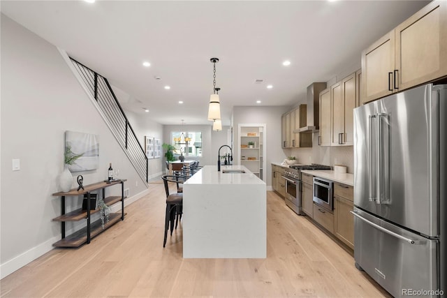 kitchen with a kitchen island with sink, wall chimney range hood, sink, pendant lighting, and high quality appliances