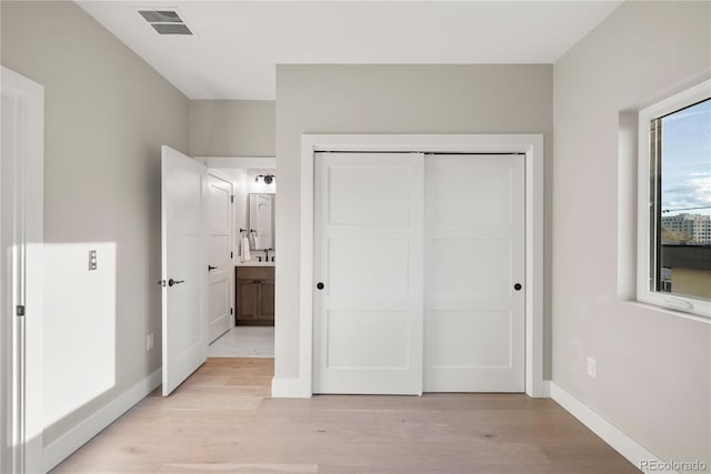 unfurnished bedroom featuring ensuite bath, a closet, and light wood-type flooring