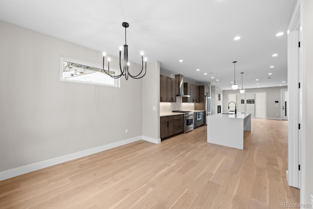 kitchen featuring a center island with sink, hanging light fixtures, dark brown cabinets, stainless steel appliances, and wall chimney range hood