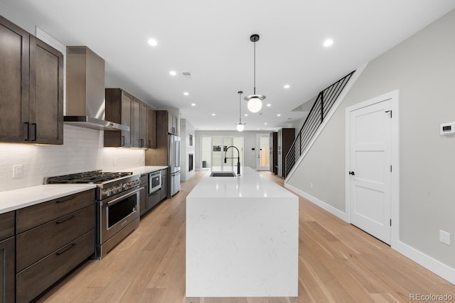 kitchen featuring sink, high quality appliances, a kitchen island, decorative light fixtures, and wall chimney range hood