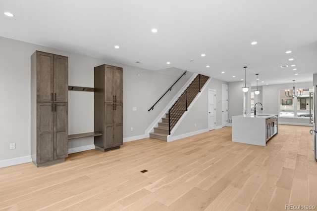 unfurnished living room with sink, an inviting chandelier, and light hardwood / wood-style floors