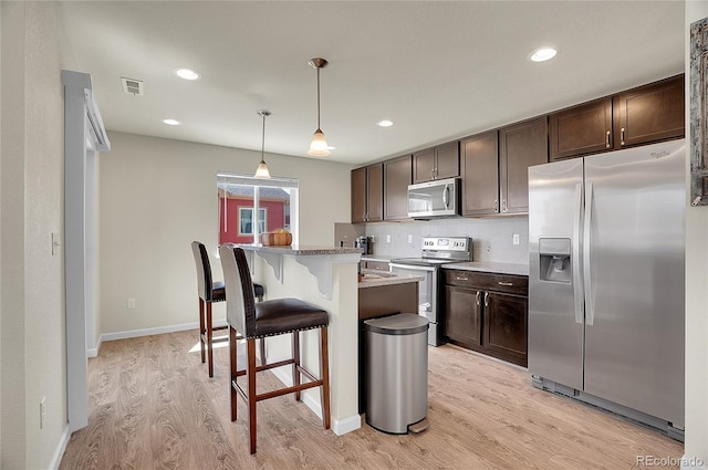 kitchen featuring pendant lighting, appliances with stainless steel finishes, dark brown cabinets, a kitchen island, and a kitchen bar