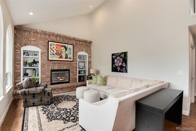 11056 W Rowland Ave, Littleton, CO 80127 - living room featuring vaulted ceiling, built in features, wood finished floors, a brick fireplace, and baseboards