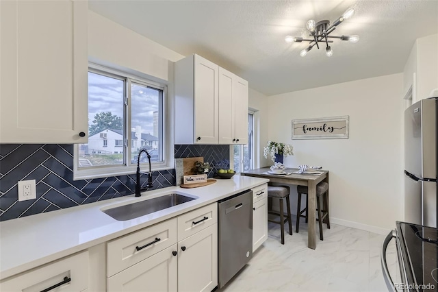 kitchen with tasteful backsplash, white cabinetry, sink, stainless steel appliances, and an inviting chandelier