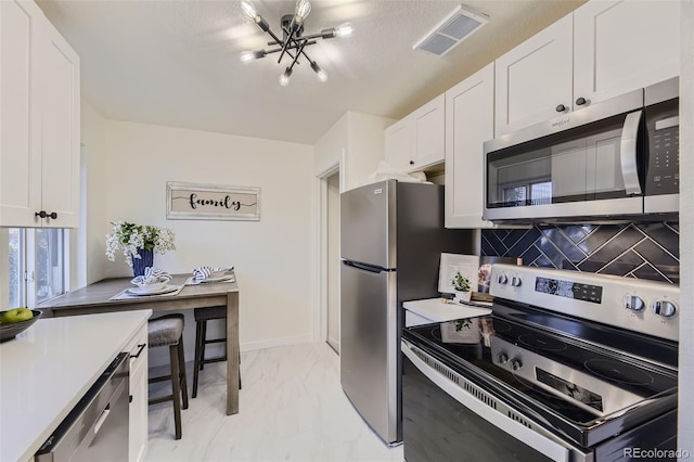 kitchen featuring white cabinetry, backsplash, stainless steel appliances, and an inviting chandelier