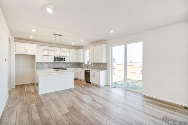 kitchen with white cabinets, a kitchen island, appliances with stainless steel finishes, light hardwood / wood-style floors, and decorative light fixtures