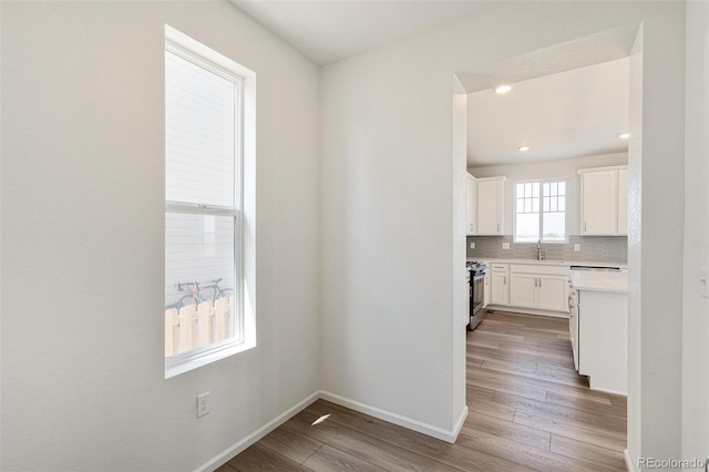 kitchen with white cabinets, stainless steel stove, light wood-type flooring, and backsplash