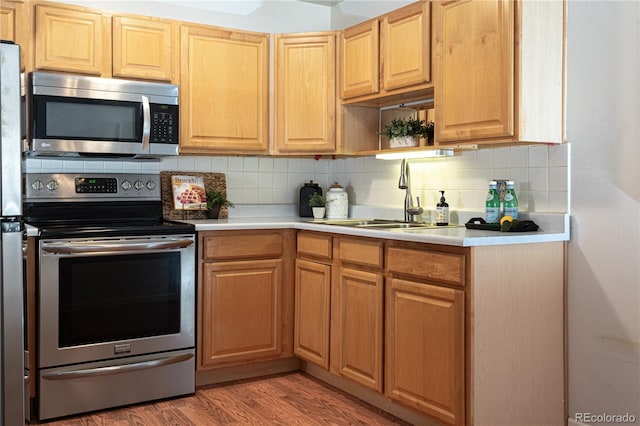 kitchen with stainless steel appliances, a sink, light wood-style floors, light countertops, and backsplash