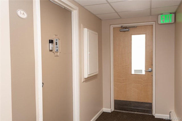 corridor featuring dark colored carpet, a baseboard radiator, a paneled ceiling, and baseboards