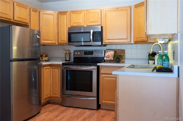 kitchen featuring light wood finished floors, decorative backsplash, appliances with stainless steel finishes, light countertops, and a sink