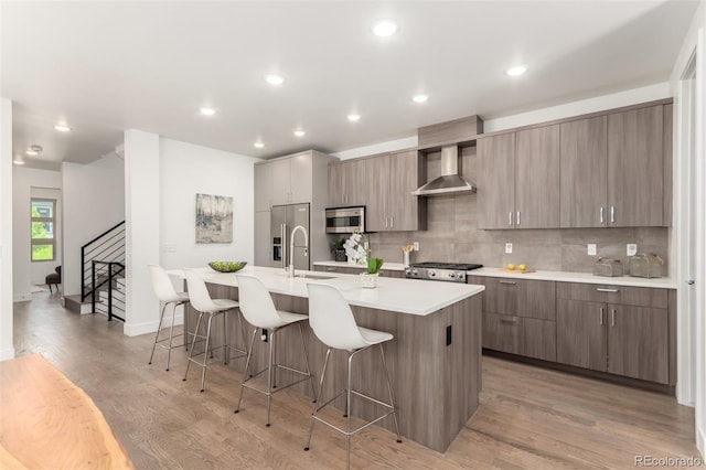 3586 S Ogden St, Englewood, CO 80113 - kitchen featuring appliances with stainless steel finishes, an island with sink, wall chimney range hood, a breakfast bar area, and light countertops