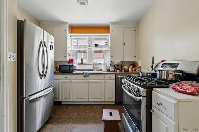 kitchen with appliances with stainless steel finishes, a sink, white cabinetry, and stone finish flooring