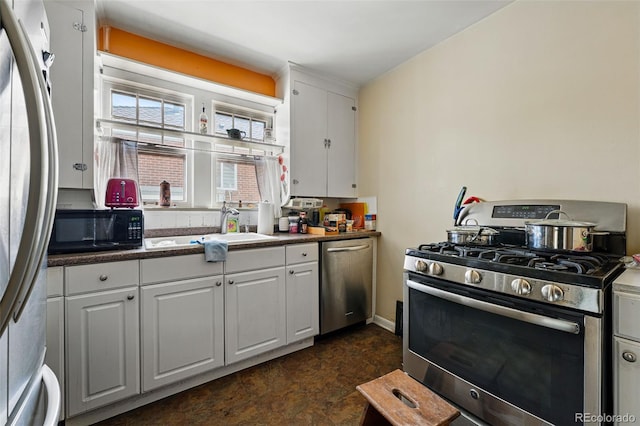 kitchen with stainless steel appliances, white cabinets, dark countertops, and a sink