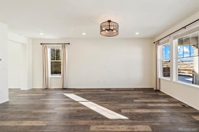 empty room with baseboards, dark wood-type flooring, a notable chandelier, and recessed lighting