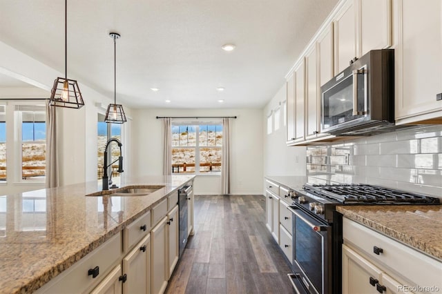 kitchen with light stone counters, a sink, range with gas stovetop, backsplash, and pendant lighting