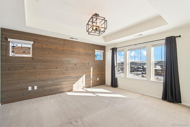 unfurnished room with light carpet, a tray ceiling, wood walls, and visible vents