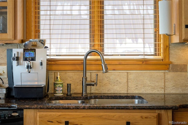 kitchen with brown cabinetry, glass insert cabinets, dark stone counters, and a sink