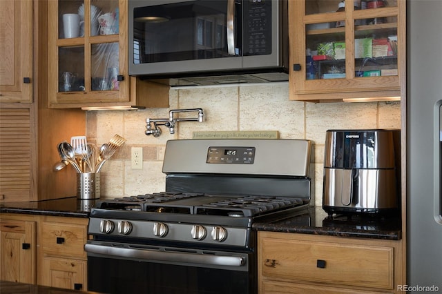 kitchen featuring tasteful backsplash, dark stone counters, glass insert cabinets, brown cabinets, and appliances with stainless steel finishes