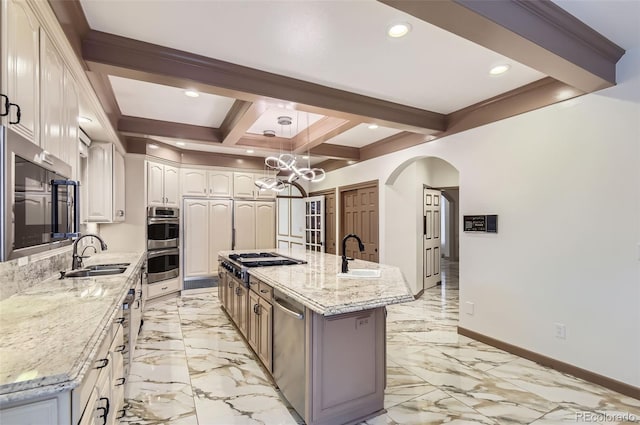 kitchen with sink, a kitchen island with sink, beam ceiling, coffered ceiling, and light stone counters