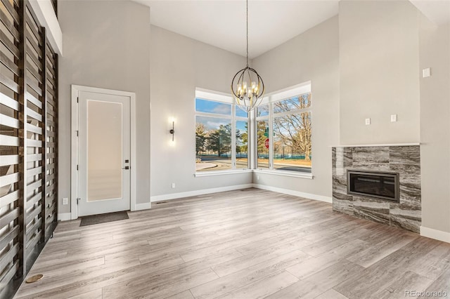 unfurnished living room featuring a towering ceiling, light hardwood / wood-style flooring, a notable chandelier, and a tiled fireplace