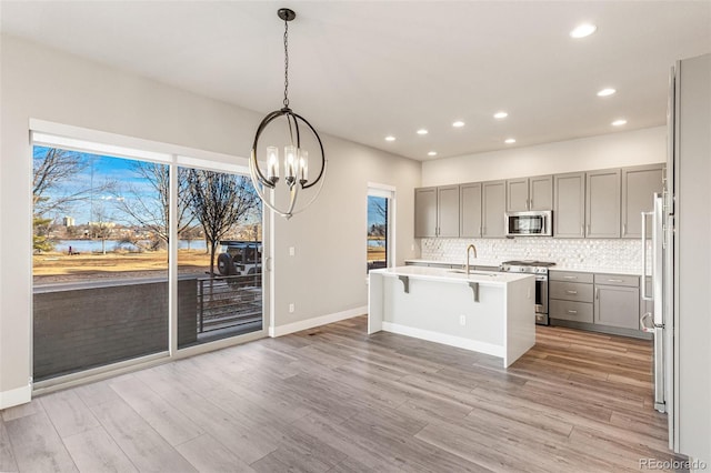 kitchen with tasteful backsplash, decorative light fixtures, a center island with sink, high quality appliances, and gray cabinets