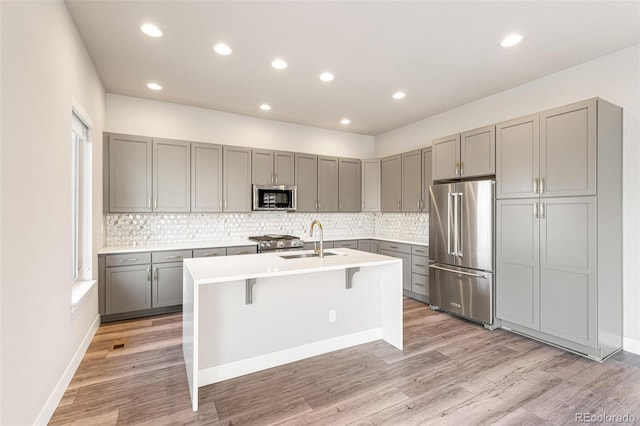 kitchen with gray cabinetry, sink, an island with sink, a kitchen bar, and stainless steel appliances