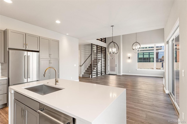 kitchen with appliances with stainless steel finishes, gray cabinetry, sink, a center island with sink, and a chandelier