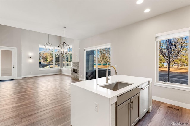 kitchen featuring stainless steel dishwasher, sink, an inviting chandelier, hanging light fixtures, and an island with sink