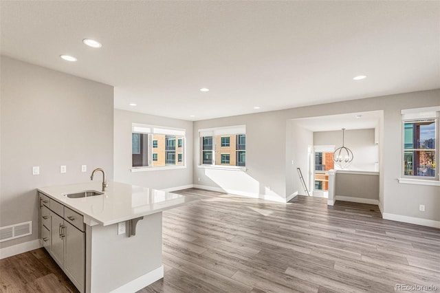 kitchen with kitchen peninsula, sink, pendant lighting, light hardwood / wood-style flooring, and a notable chandelier