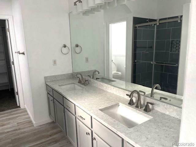11282 Osage Cir N Unit F, Northglenn, CO 80234 - full bathroom with wood finished floors, double vanity, toilet, baseboards, and a shower with door