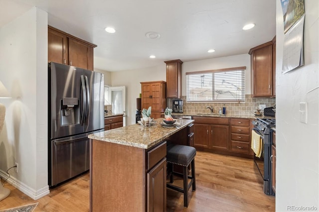 kitchen with stainless steel refrigerator with ice dispenser, black gas stove, a breakfast bar, a kitchen island, and light wood-type flooring