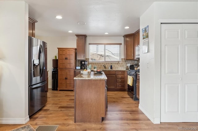 kitchen with a center island, black gas stove, stainless steel refrigerator with ice dispenser, light hardwood / wood-style floors, and light stone counters