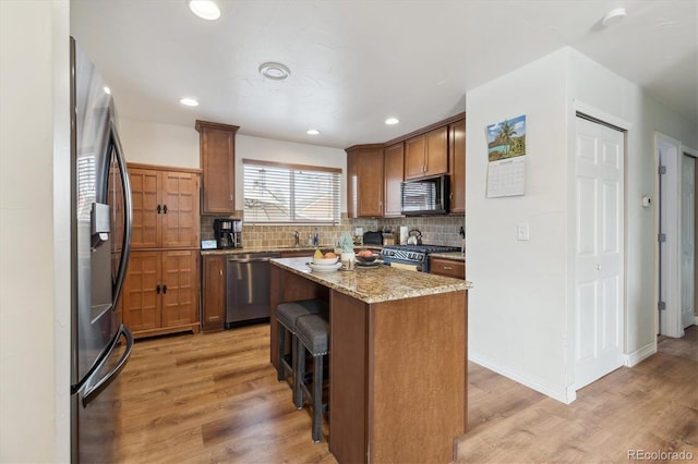 kitchen featuring a center island, stainless steel appliances, light stone counters, light hardwood / wood-style floors, and a breakfast bar area