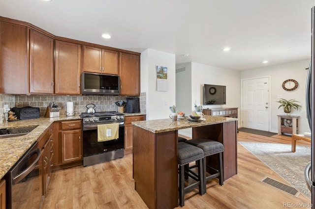 kitchen featuring light stone countertops, a center island, stainless steel appliances, light hardwood / wood-style flooring, and decorative backsplash