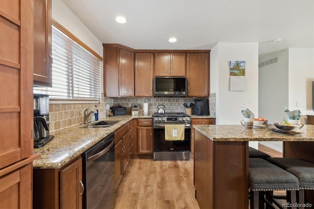 kitchen with light stone countertops, a breakfast bar, light wood-type flooring, and appliances with stainless steel finishes