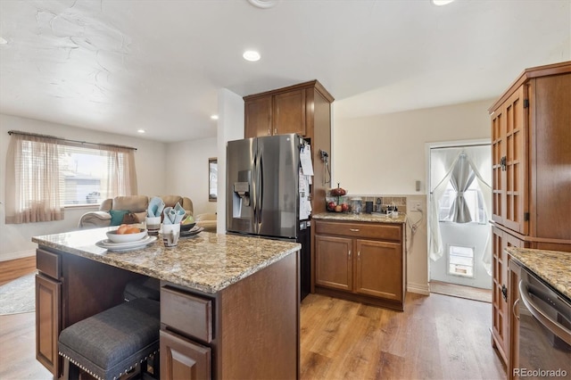 kitchen featuring a kitchen breakfast bar, light stone counters, light hardwood / wood-style floors, and appliances with stainless steel finishes