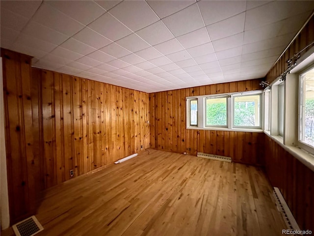 unfurnished room with wooden walls, a baseboard radiator, and light hardwood / wood-style floors