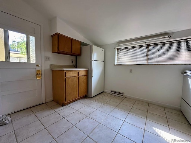 kitchen with vaulted ceiling, white fridge, and light tile patterned floors