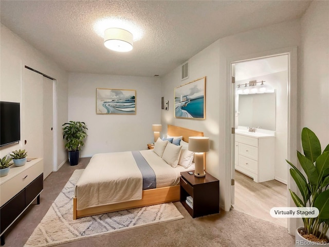 bedroom featuring ensuite bath, carpet flooring, and a textured ceiling