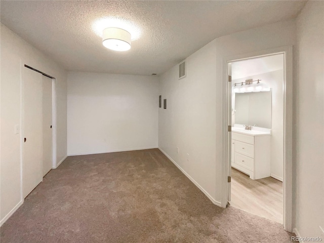 unfurnished bedroom featuring ensuite bath, light colored carpet, a closet, and a textured ceiling