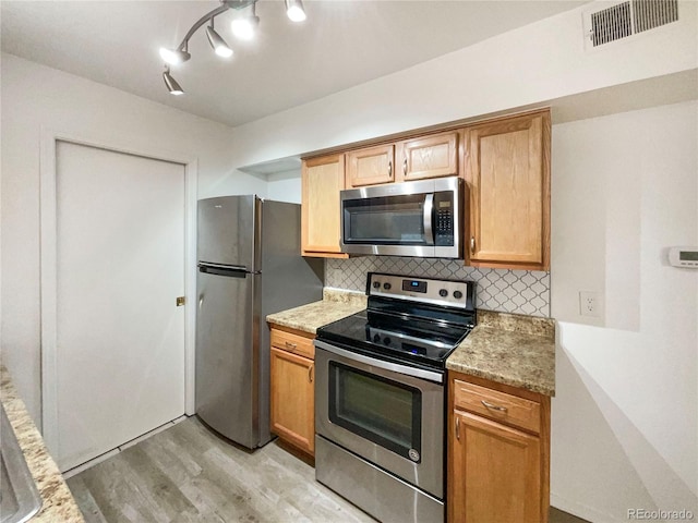 kitchen with stainless steel appliances, light stone countertops, decorative backsplash, and light wood-type flooring